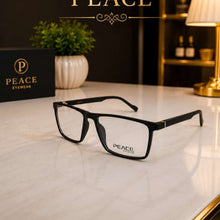 Load image into Gallery viewer, Black rectangular eyeglasses with clear lenses resting on a white marble surface, with the PEACE brand name visible on the frame and a matching PEACE box beside it in a styled interior setting.